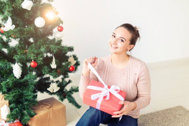 christmas, x-mas, winter, happiness concept - girl opens a gift against the background of the Christmas tree. Happy young woman celebrating Christmas