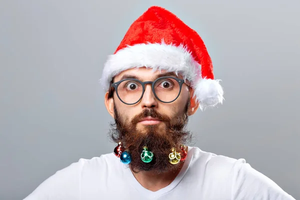 Christmas, holidays, barbershop and style concept - young handsome bearded santa claus man with many small christmas baubles in long beard — Stok fotoğraf
