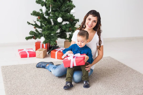 クリスマス、シングル親と休日のコンセプト-かわいい男の子開催クリスマスプレゼントのために彼の母親に家. — ストック写真