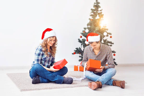 Ünnepek, karácsony és családi koncepció - Fiatal boldog pár ajándékokat nyit otthon. — Stock Fotó