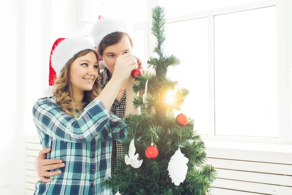 Család, x-mas, téli ünnepek és emberek koncepció - boldog fiatal pár díszítő karácsonyfa otthon — Stock Fotó