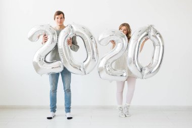 Bayramlar, şenlik ve parti konsepti mutlu çift öpücükleri ve beyaz arka planda gümüş 2020 balon tutmaları. Yeni yıl kutlaması