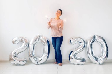 New Year celebration and party concept - Happy young woman with sparklers near silver 2020 balloons on white background.