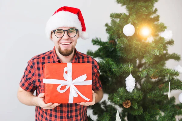 Kerstmis en feestdagen concept - Grappige man in santa hoed met een geschenk thuis in de woonkamer — Stockfoto