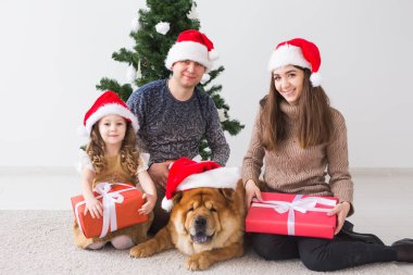 Evcil hayvan, tatil ve festival konsepti - Köpekli aile yılbaşı ağacının yanında oturuyor.