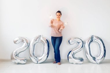 New Year celebration and party concept - Happy young woman with sparklers near silver 2020 balloons on white background.