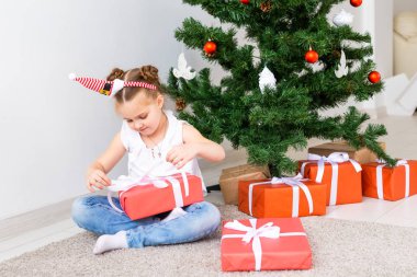Çocuk Noel hediyelerini açıyor. Noel ağacının altında hediye kutularıyla çocuk.