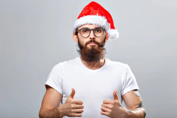 Concepto de vacaciones y personas - Retrato de un hombre guapo y brutal en sombrero de Navidad. Sobre fondo gris . —  Fotos de Stock