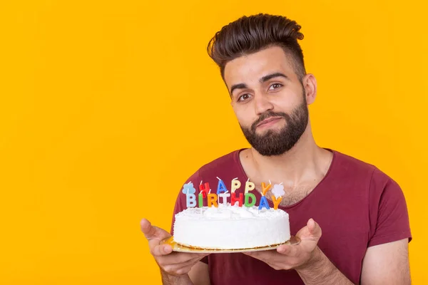 Young male hipster with a beard holding a cake with the inscription happy birthday congratulations on the anniversary and the holiday. Concept of promotions and discounts. Copy space