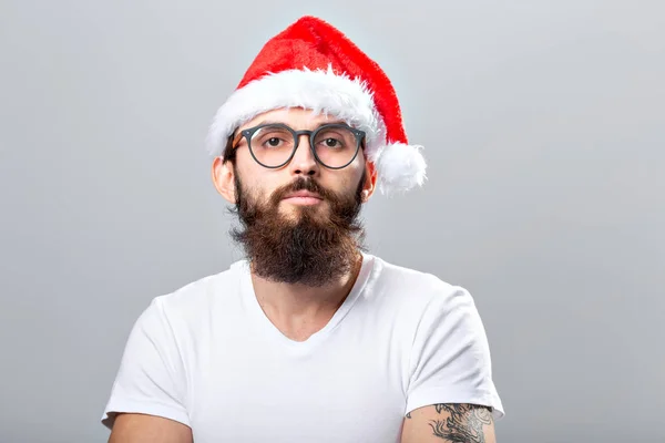 Holidays and people concept - Portret van een knappe brutale man met kerstmuts. Over grijze achtergrond. — Stockfoto