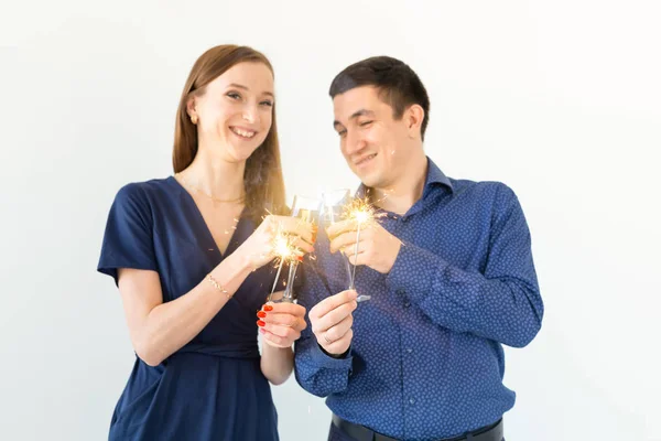 Homem e mulher comemorando a festa de Natal ou Ano Novo com luzes de Bengala e copos de champanhe no fundo branco . — Fotografia de Stock
