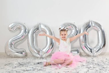 Yeni yıl, tatiller ve kutlama konsepti - 2020 numaralı balonlarla birlikte oturan küçük kız