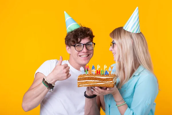 젊은 쾌활한 학생 매력적인 소녀와 케이크를 들고 종이 모자를 인사하는 좋은 사람. 생일과 기념일에 축 하의 개념 — 스톡 사진