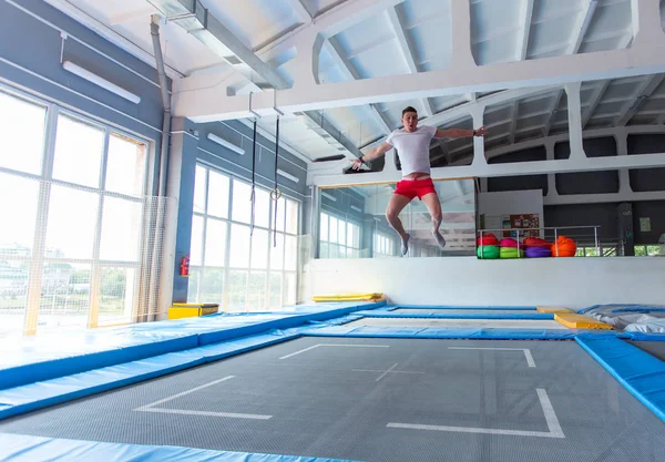 Fitness, diversão, lazer e esporte conceito de atividade - Bonito homem feliz pulando em um trampolim dentro de casa — Fotografia de Stock