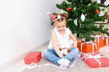 Çocuk Noel hediyelerini açıyor. Noel ağacının altında hediye kutularıyla çocuk.