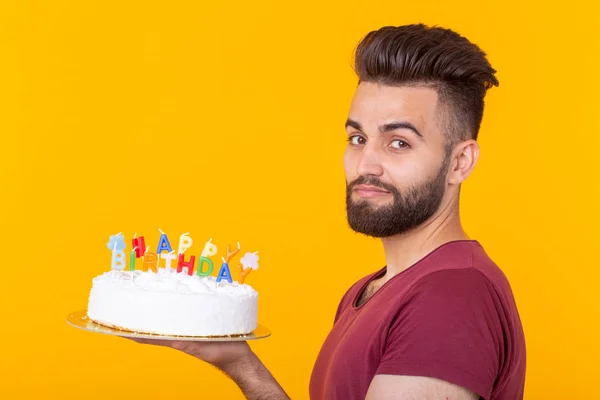 Young male hipster with a beard holding a cake with the inscription happy birthday congratulations on the anniversary and the holiday. Concept of promotions and discounts.