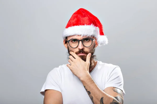 Holidays and people concept - Portret van een knappe brutale man met kerstmuts. Over grijze achtergrond. — Stockfoto