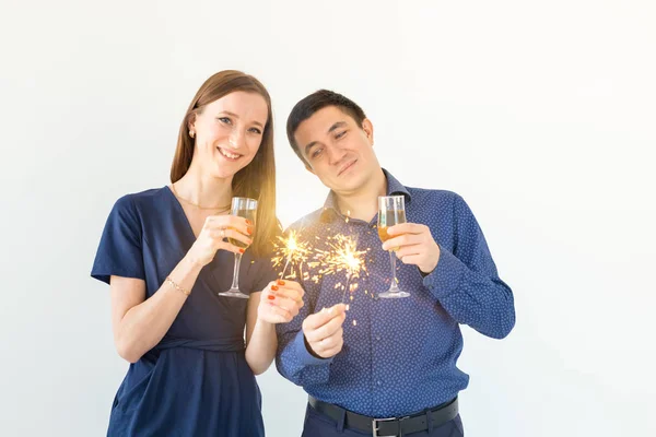 Hombre y mujer celebrando la fiesta de Navidad o Año Nuevo con luces de Bengala y copas de champán sobre fondo blanco . — Foto de Stock