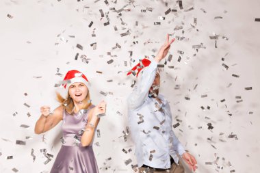 Yeni yıl, Noel ve parti konsepti - Neşeli gençler beyaz arka planda konfeti yağmuruna tutuldu.