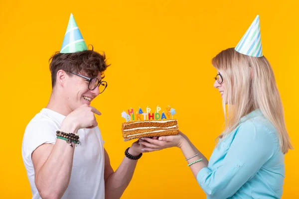 재미 괴상한 남자와 여자는 노란색 배경 위에 촛불과 생일 케이크를 들고 휴일 모자와 안경을 착용 — 스톡 사진