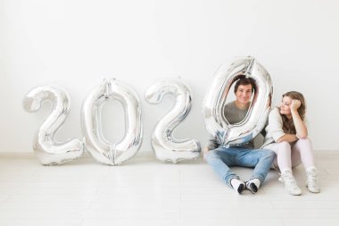 Tatiller, şenlik ve parti konsepti. Beyaz arka planda, gümüş 2020 balon yakınında oturan komik bir çift. Yeni yıl kutlaması