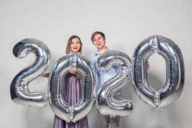 Yeni yıl, kutlama ve tatil kavramı. Yeni yıl için gümüş balonlardan yapılmış 2020 tabelasıyla eğlenen aşk çifti.