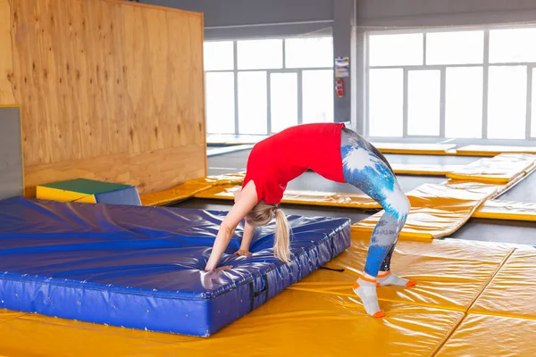 Jovem esportista em um trampolim no parque de fitness e fazendo exercício dentro de casa — Fotografia de Stock