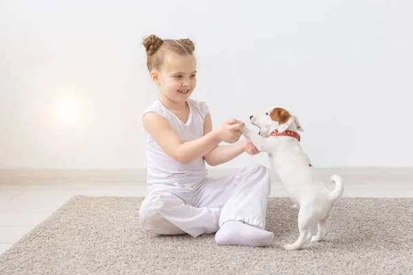Cães, crianças e animais de estimação conceito - menina criança sentada no chão com filhote de cachorro bonito — Fotografia de Stock
