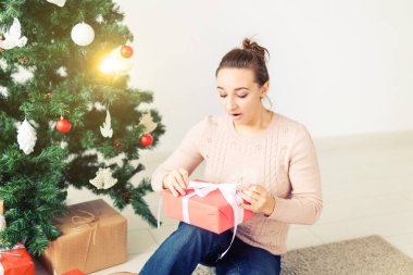 christmas, x-mas, winter, happiness concept - girl opens a gift against the background of the Christmas tree. Happy young woman celebrating Christmas