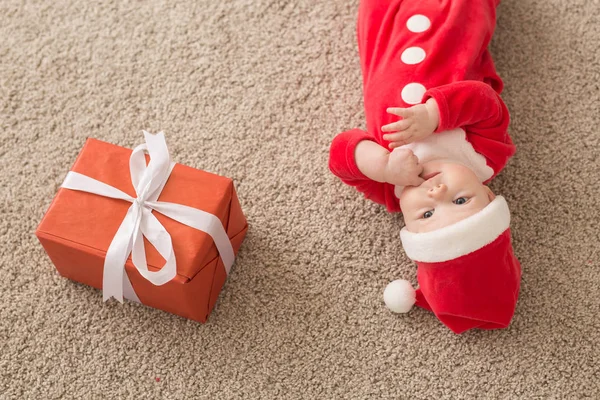 Piękne maleństwo świętuje święta. Noworoczne wakacje. Dziecko w stroju świątecznym i w Santa kapelusz i pudełko prezentów, widok z góry — Zdjęcie stockowe