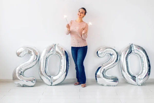 Celebración de Año Nuevo y concepto de fiesta - Mujer joven feliz con bengalas cerca de globos de plata 2020 sobre fondo blanco . — Foto de Stock