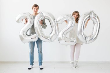 Tatiller, şenlik ve parti konsepti mutlu, eğlenceli çift, beyaz arka planda gümüş 2020 balon tutuyor. Yeni yıl kutlaması