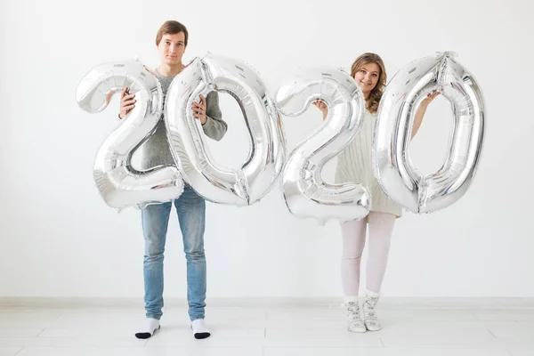 Vacaciones, festivo y concepto de fiesta - Pareja divertida amante feliz sostiene globos de plata 2020 sobre fondo blanco. Celebración de Año Nuevo — Foto de Stock