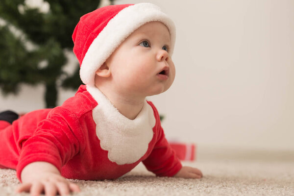 Милая малышка в костюме Санта Клауса ползает по полу над елкой. Праздничный сезон
.