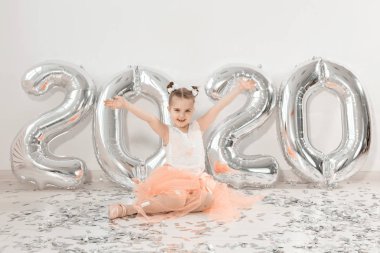 Yeni yıl, tatiller ve kutlama konsepti - 2020 numaralı balonlarla birlikte oturan küçük kız