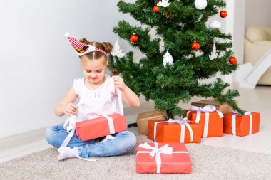 Çocuk Noel hediyelerini açıyor. Noel ağacının altında hediye kutularıyla çocuk.