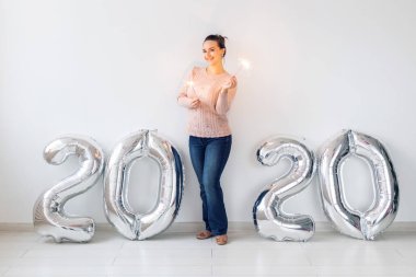New Year celebration and party concept - Happy young woman with sparklers near silver 2020 balloons on white background.
