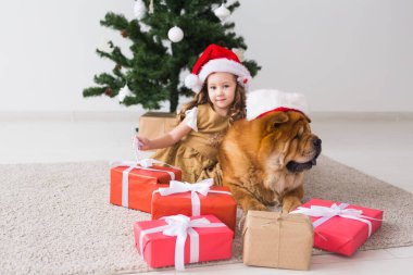 Çocuklar ve evcil hayvan konsepti. Noel ağacının yanında oturan köpekli tatlı kız. Mutlu Noeller ve mutlu tatiller.