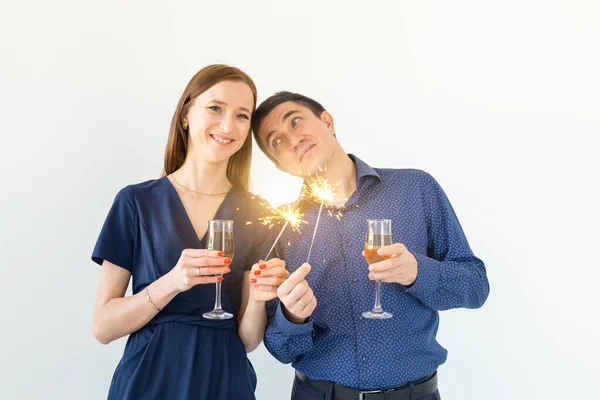 Uomo e donna che festeggiano il Natale o il Capodanno con luci del Bengala e bicchieri di champagne su sfondo bianco . — Foto Stock