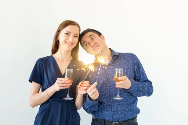 Homem e mulher comemorando a festa de Natal ou Ano Novo com luzes de Bengala e copos de champanhe no fundo branco . — Fotografia de Stock