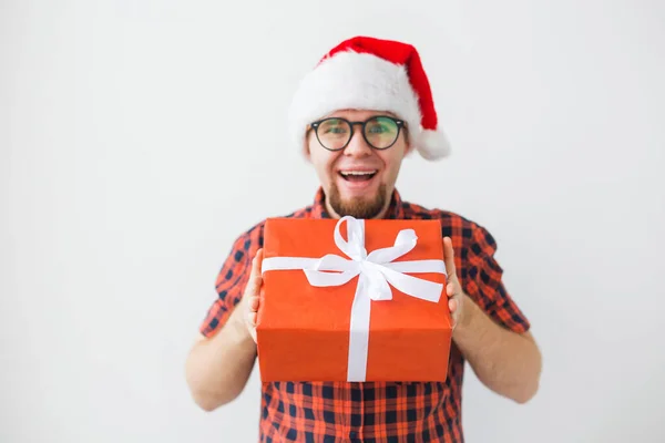 Concepto de Navidad y vacaciones - Hombre divertido en sombrero de santa celebración de un regalo sobre fondo blanco —  Fotos de Stock