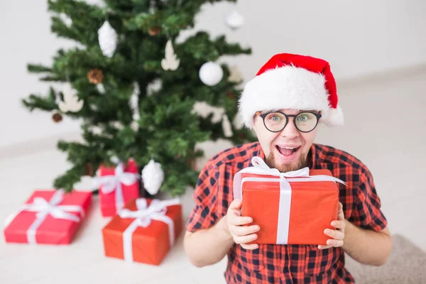 Conceito de Natal e feriados - Homem engraçado em santa chapéu segurando um presente em casa na sala de estar — Fotografia de Stock