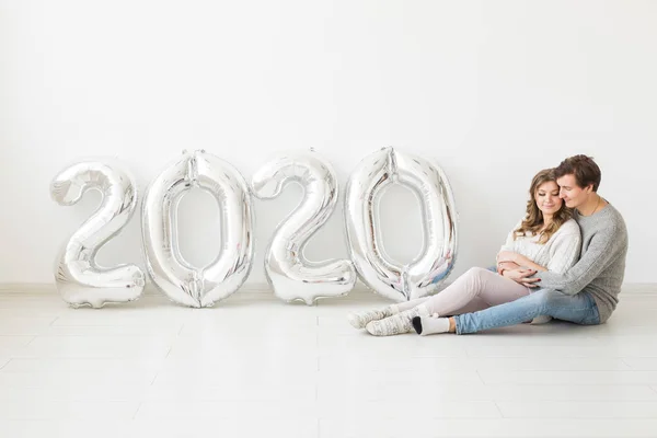 축일, 축제 및 파티 개념 - 행복하고 사랑에 찬 부부가은 2020 년의 풍선 이 있는 곳 근처 바닥에 하얀 배경을 놓고 앉아 있다. 새해 기념행사 — 스톡 사진