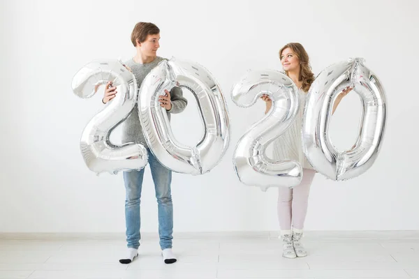 Vacaciones, festivo y concepto de fiesta - Pareja divertida amante feliz sostiene globos de plata 2020 sobre fondo blanco. Celebración de Año Nuevo — Foto de Stock