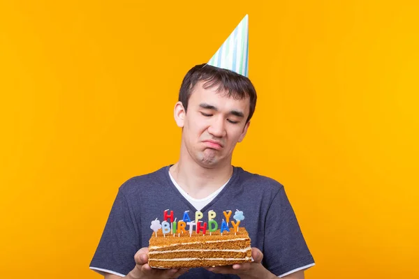 Fou joyeux jeune asiatique avec des lunettes tenant une bougie brûlante dans ses mains et un gâteau maison félicitant sur un fond jaune. Concept de célébration anniversaire et anniversaire . — Photo