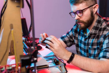 Laboratuvarda 3D yazıcı kullanan ve ürün prototipi, teknoloji ve yenilik kavramını inceleyen genç bir erkek tasarımcı.