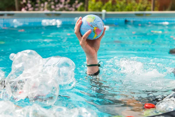 UFA, RUSSIA - JULY 25, 2019 : Problem of trash, plastic recycling, pollution and environmental concept - Plastic rubbish pollution in water environment, Earth globe is floating in the trash