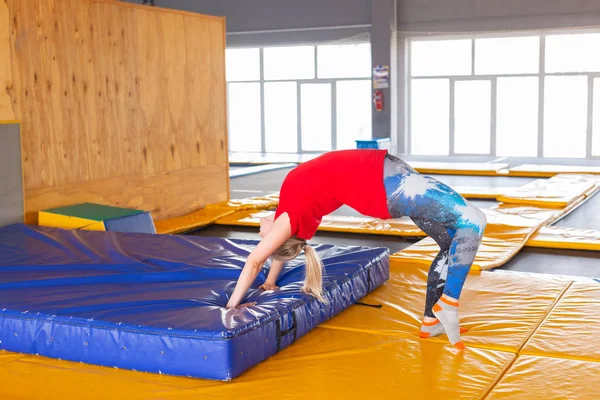 Perempuan muda olahragawan di atas trampolin di taman kebugaran dan melakukan olahraga di dalam ruangan — Stok Foto
