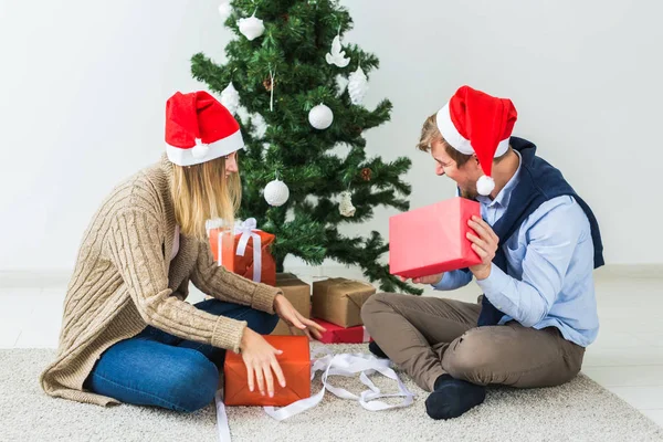 クリスマスと休日のコンセプト-若い幸せなカップルはサンタの帽子をかぶって家で贈り物を開く. — ストック写真