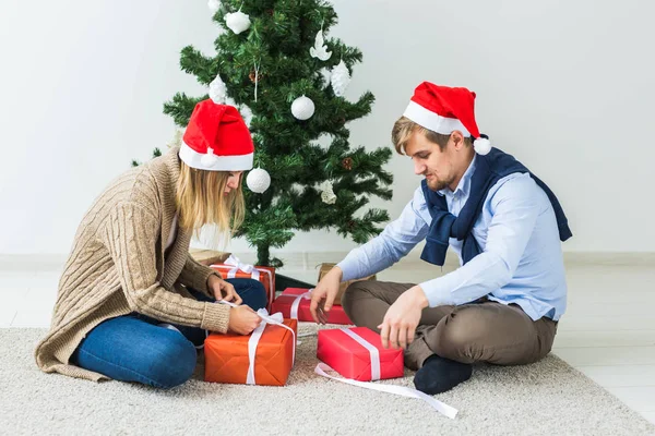 Концепция Рождества и праздников - Молодая счастливая пара в шапках Санты, открывающая подарки дома . — стоковое фото